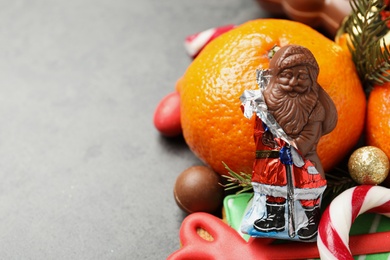 Photo of Chocolate Santa Claus, Christmas sweets and tangerine on grey table, closeup. Space for text