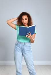 Beautiful African-American woman reading book near light wall indoors