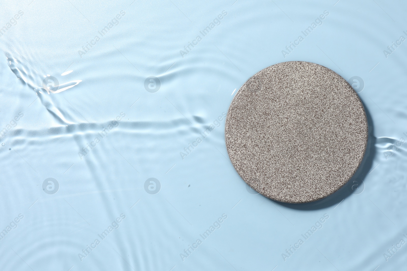 Photo of Presentation of product. Stone podium in water on light blue background, top view. Space for text