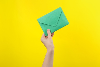 Woman holding green paper envelope on yellow background, closeup