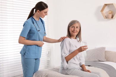 Photo of Senior woman with glass of water and young healthcare worker indoors