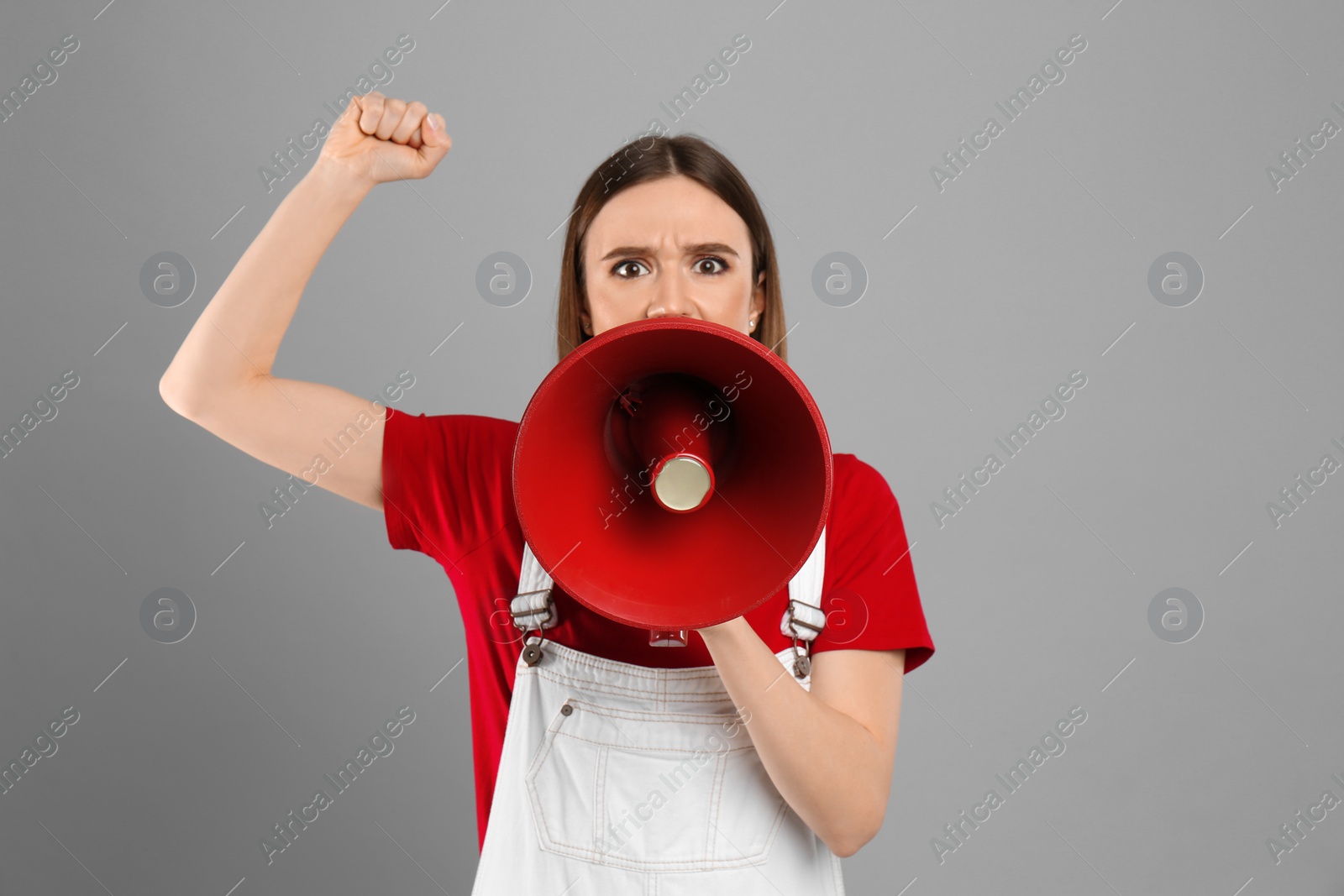 Photo of Emotional young woman with megaphone on light grey background