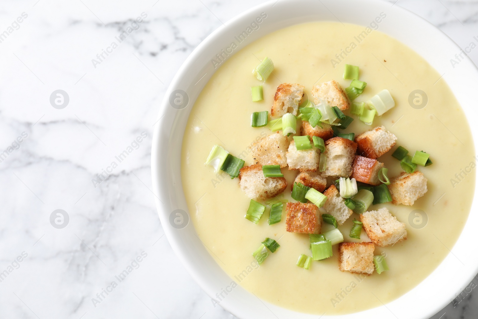 Photo of Tasty potato soup with croutons and green onion in bowl on white marble table, top view. Space for text