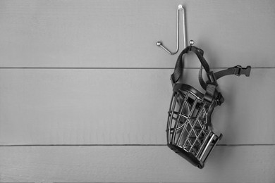 Photo of Black plastic dog muzzle hanging on gray wooden wall, space for text