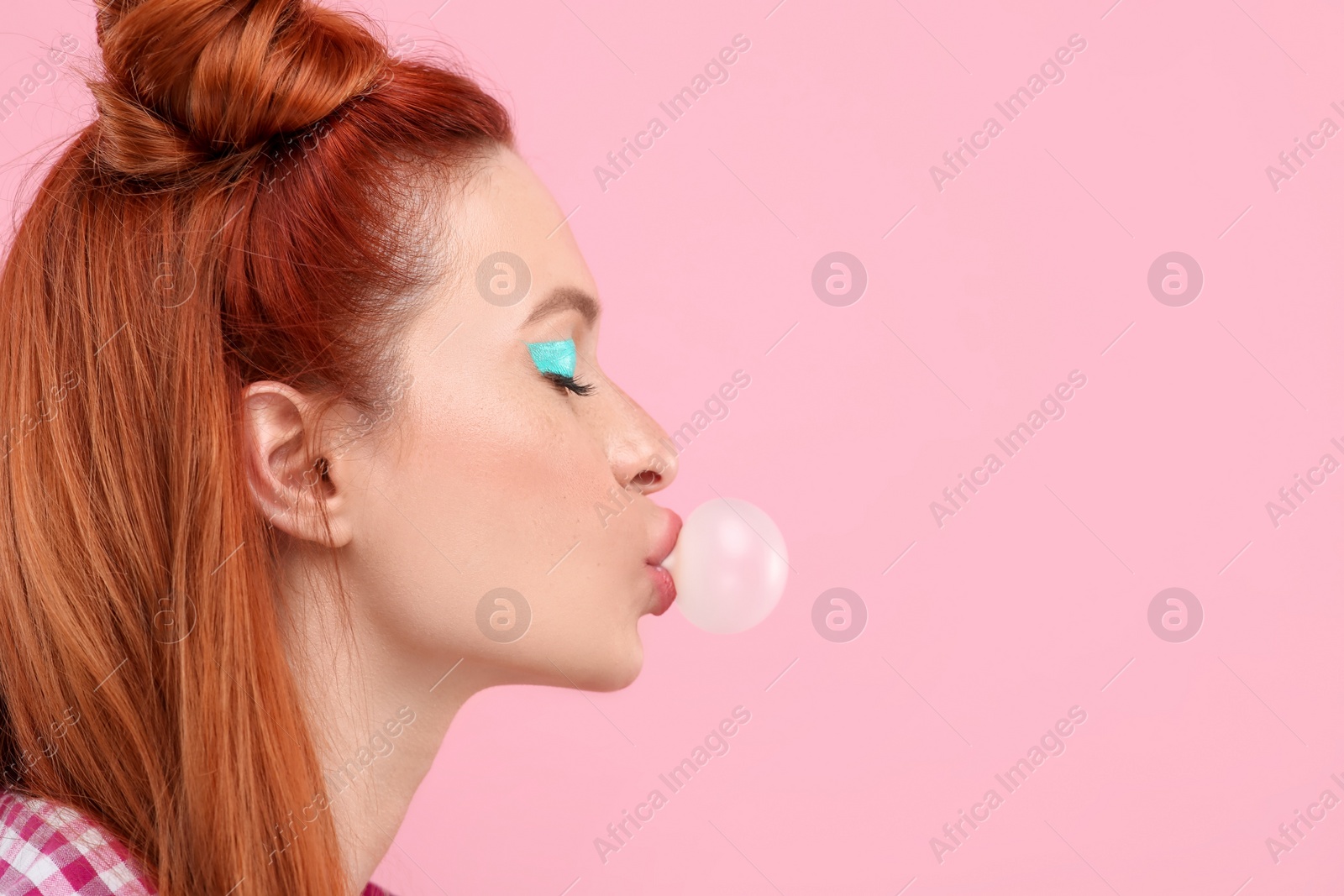 Photo of Beautiful woman with bright makeup blowing bubble gum on pink background. Space for text