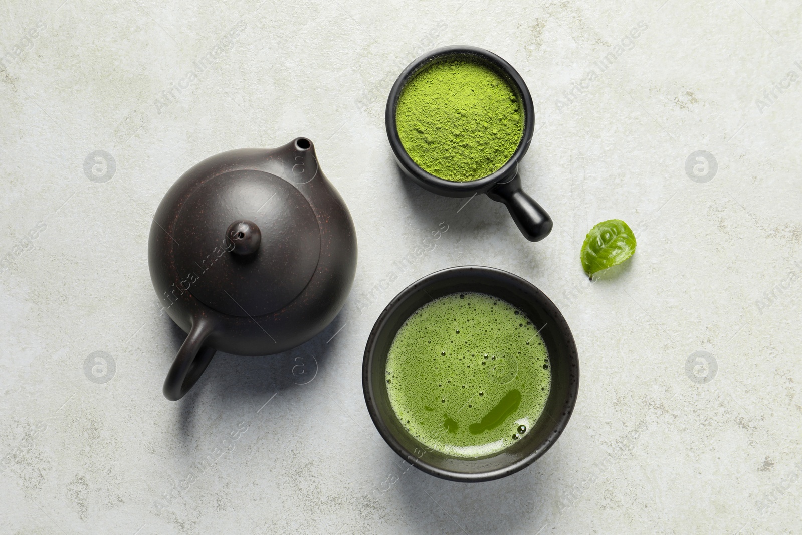 Photo of Cup of fresh matcha tea, teapot and green powder on light grey table, flat lay