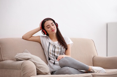 Photo of Young woman in headphones enjoying music on sofa at home