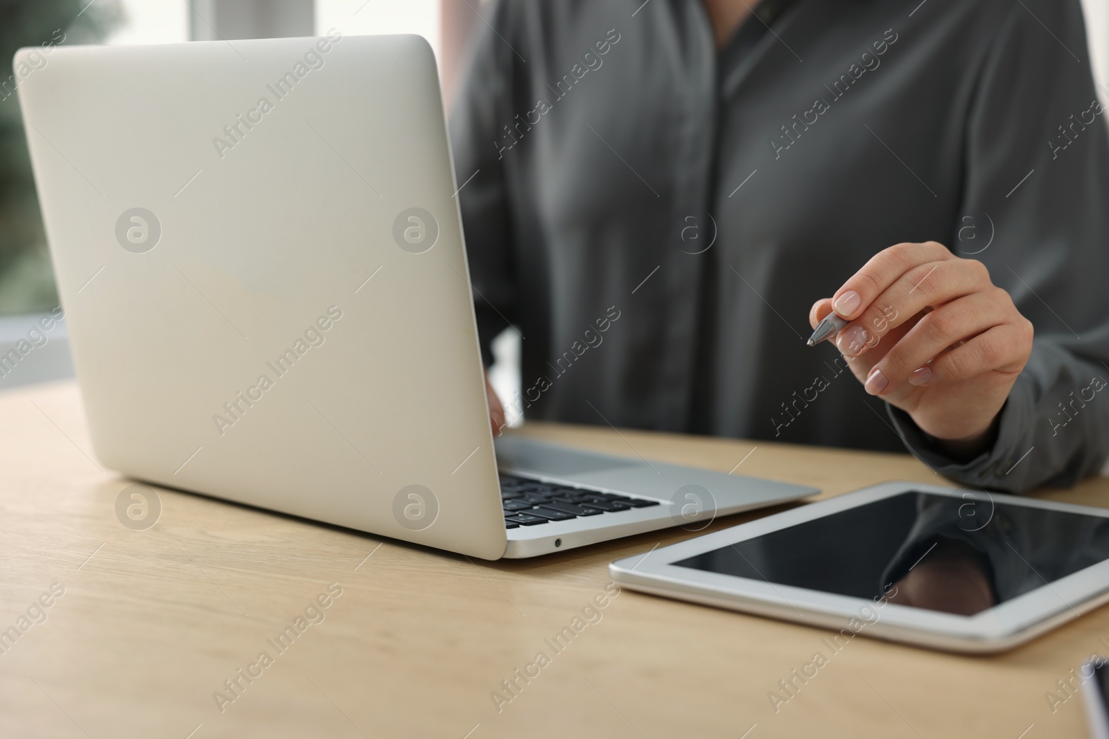 Photo of Woman with tablet and pen working on laptop at wooden table, closeup. Electronic document management