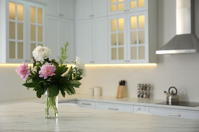 Photo of Peony bouquet on white marble table in kitchen interior