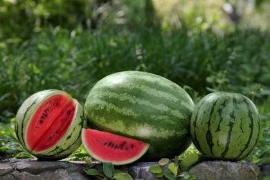 Photo of Different delicious ripe watermelons on stone surface outdoors
