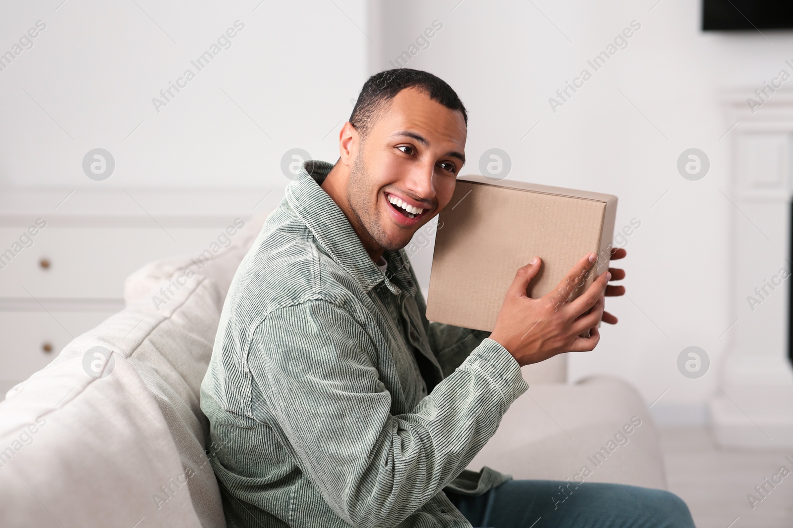 Photo of Happy young man with parcel at home. Internet shopping