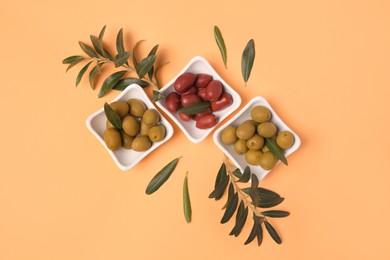 Photo of Different fresh olives and green leaves on pale orange background, flat lay
