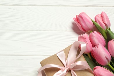 Happy Mother's Day. Beautiful pink tulips and gift box on white wooden table, flat lay. Space for text