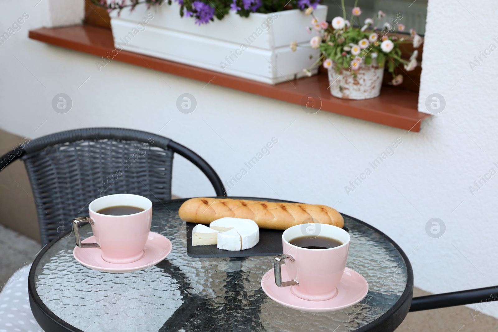 Photo of Cups of coffee, bread and cheese on glass table. Relaxing place at outdoor terrace