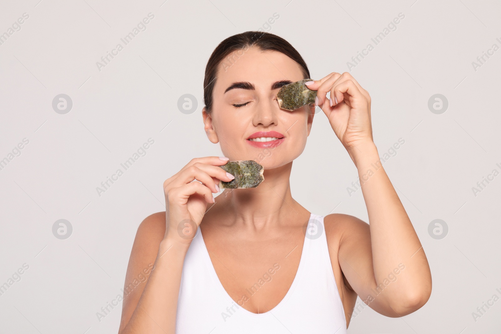 Photo of Beautiful woman applying green tea bags on skin under eyes against beige background