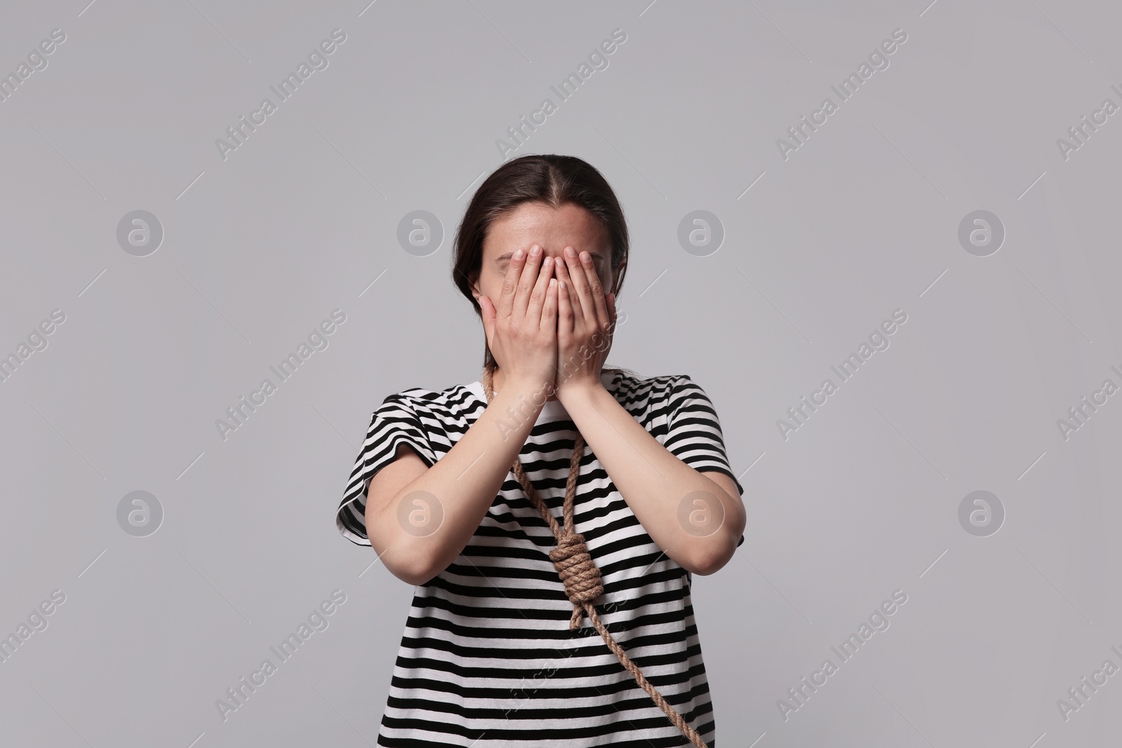 Photo of Depressed woman with rope noose on neck against light grey background