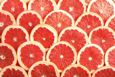 Many sliced fresh grapefruits as background, top view