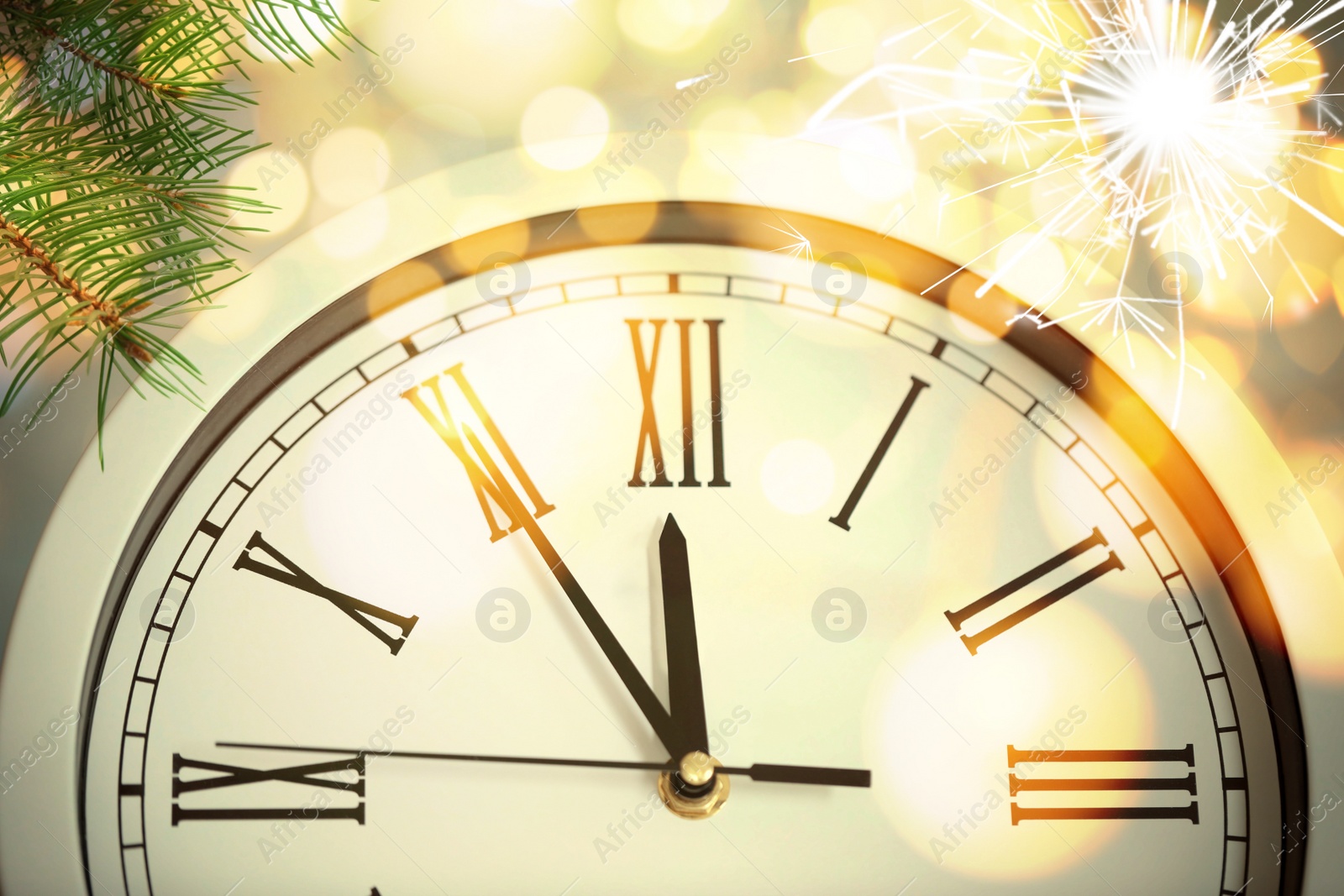 Image of Clock showing five minutes till midnight with fir tree branches and sparkler, closeup with bokeh effect. New Year countdown