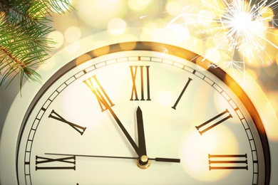 Image of Clock showing five minutes till midnight with fir tree branches and sparkler, closeup with bokeh effect. New Year countdown