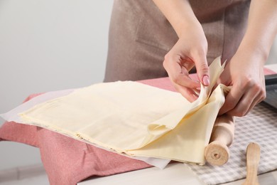 Making delicious baklava. Woman with dough at white table, closeup