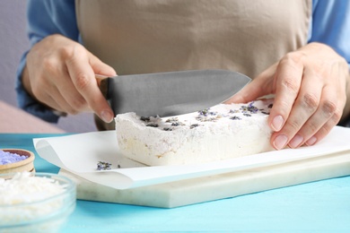 Photo of Woman cutting hand made soap bar with lavender flowers at light blue wooden table, closeup