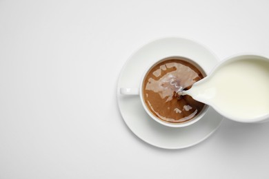 Pouring milk into cup of coffee on white background, top view