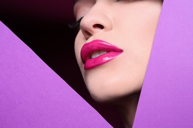 View of beautiful young woman with perfect lips makeup through cutout in color paper