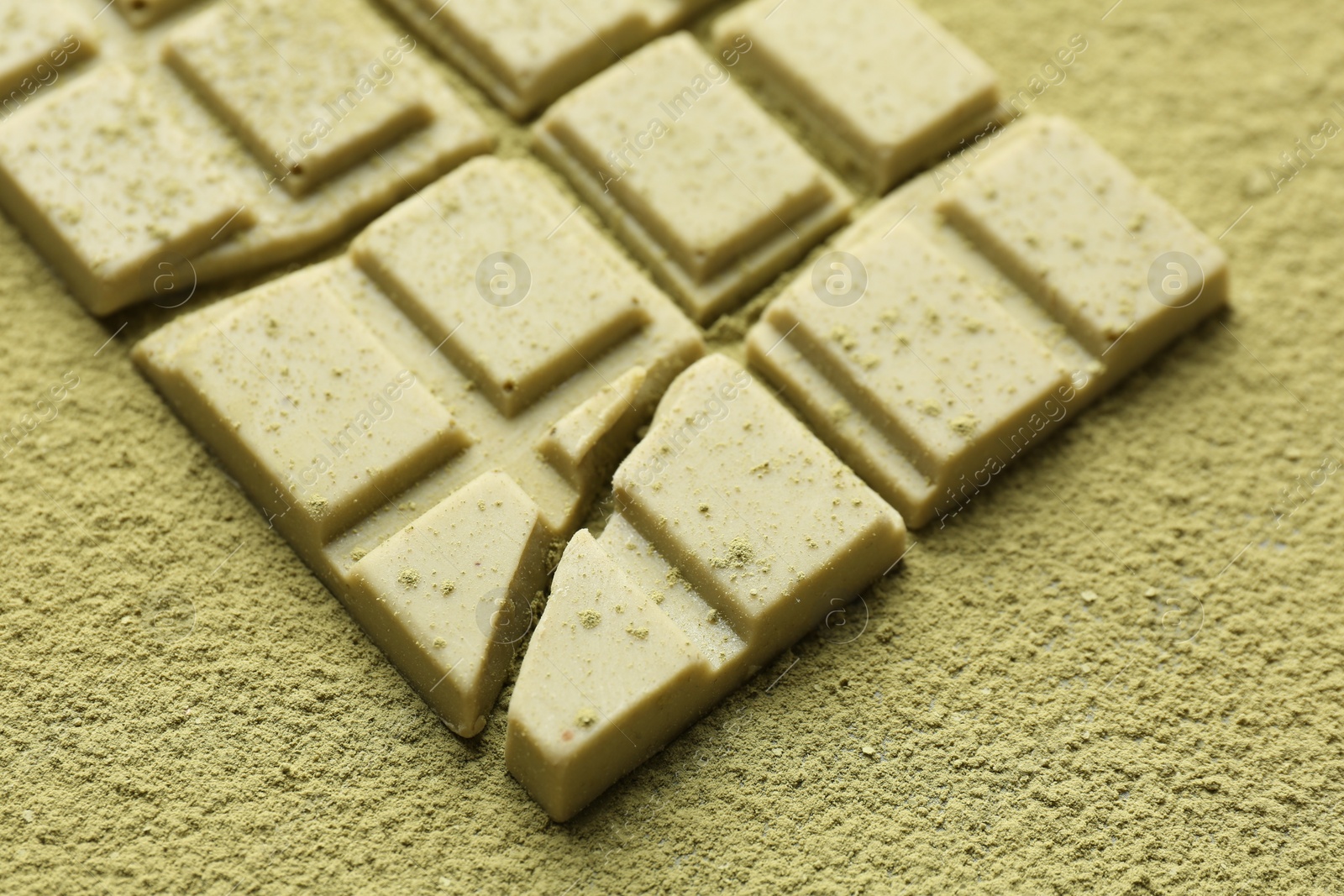 Photo of Pieces of tasty matcha chocolate bar on green powder, closeup