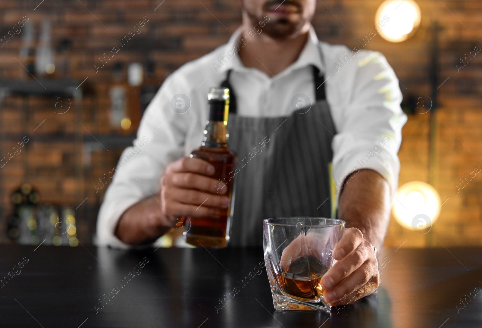 Photo of Bartender with glass and bottle of whiskey at counter in bar, closeup. Space for text