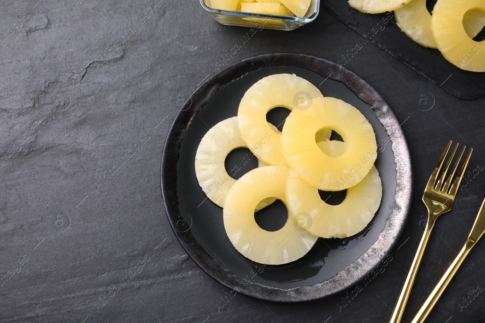 Photo of Tasty canned pineapple served on black slate table, flat lay. Space for text