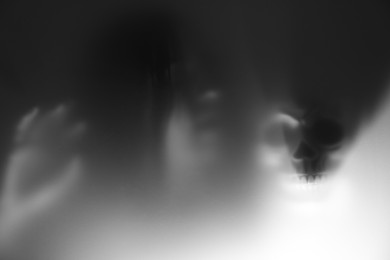 Photo of Silhouette of creepy ghost with skull behind glass against grey background