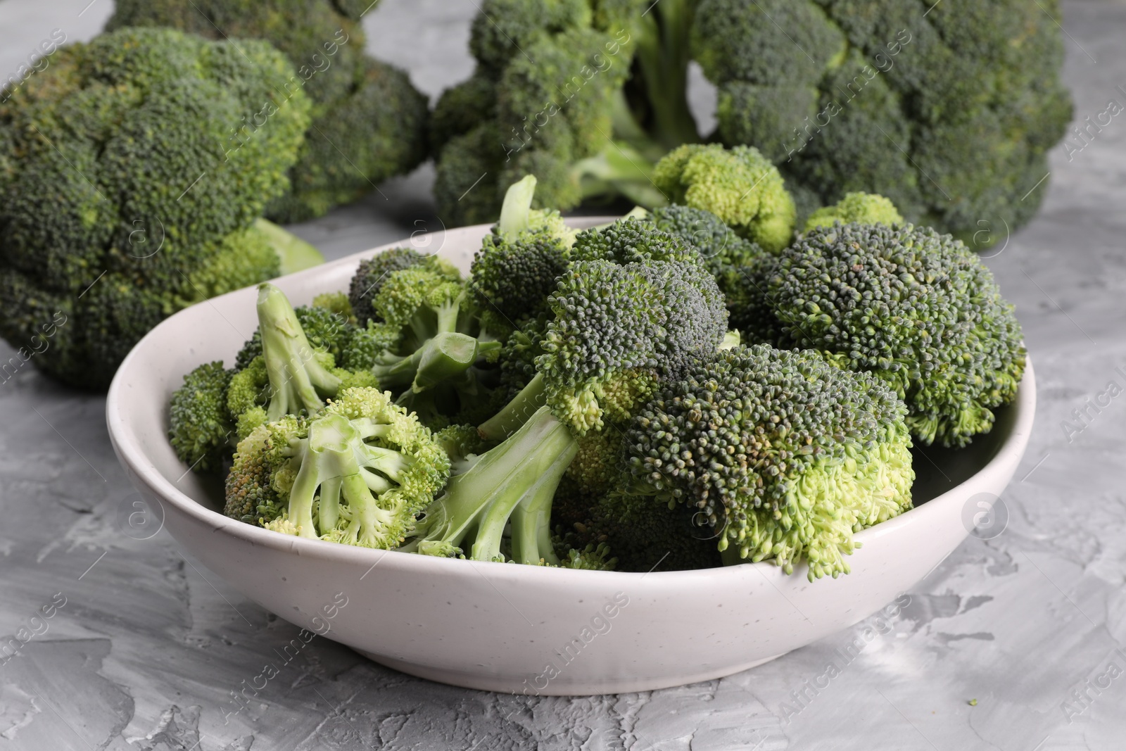 Photo of Bowl of fresh raw broccoli on grey textured table, closeup