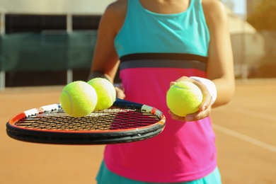 Sportswoman with racket and tennis balls at court, closeup