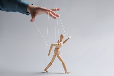 Photo of Woman pulling strings of puppet on light grey background, closeup