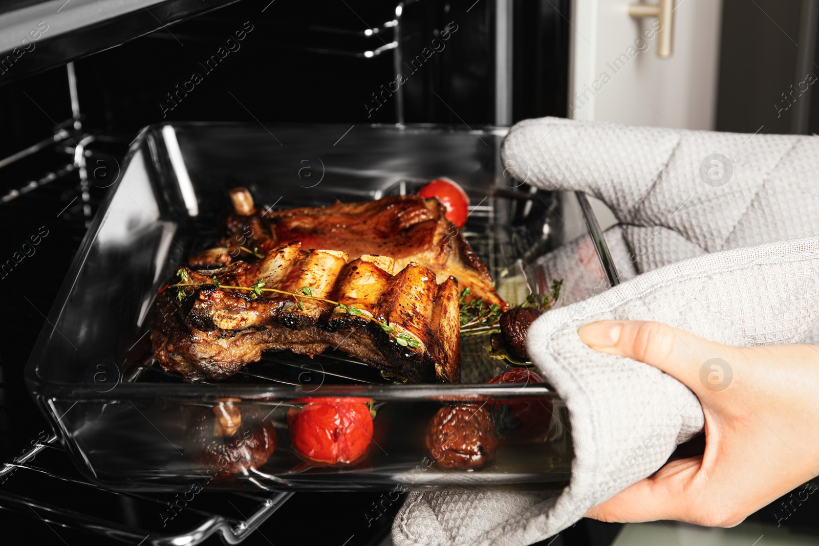 Photo of Woman taking delicious roasted ribs out of oven, closeup