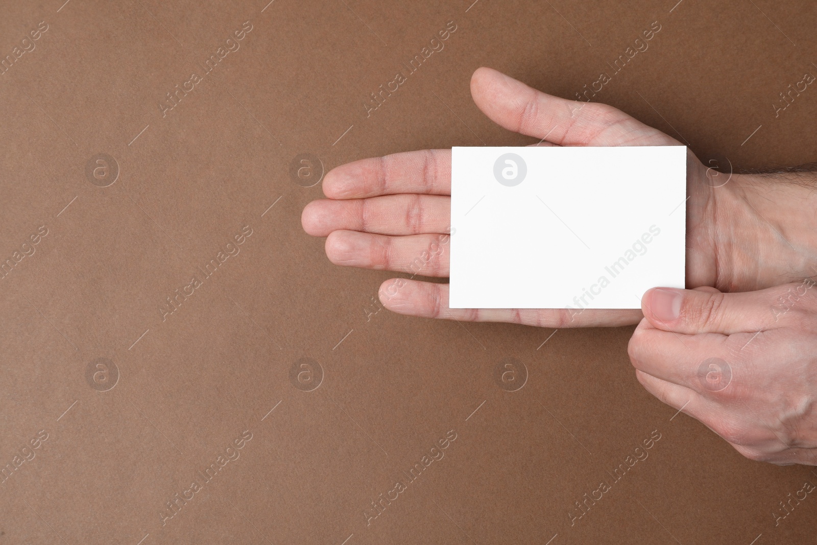 Photo of Man holding paper card on brown background, top view. Mockup for design