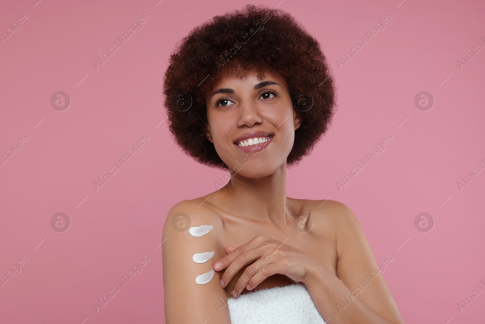 Photo of Beautiful young woman applying body cream onto arm on pink background