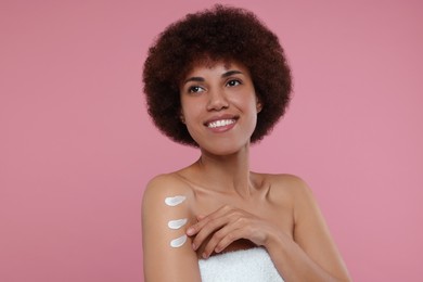 Beautiful young woman applying body cream onto arm on pink background