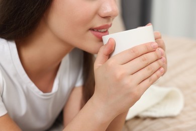 Photo of Woman drinking beverage from white ceramic mug indoors, closeup