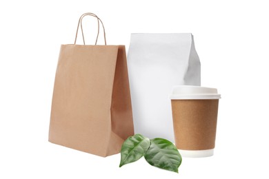 Different paper bags, coffee cup and green fresh leaves on white background, mockup for design
