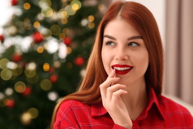 Beautiful young smiling woman against blurred lights, space for text. Celebrating Christmas