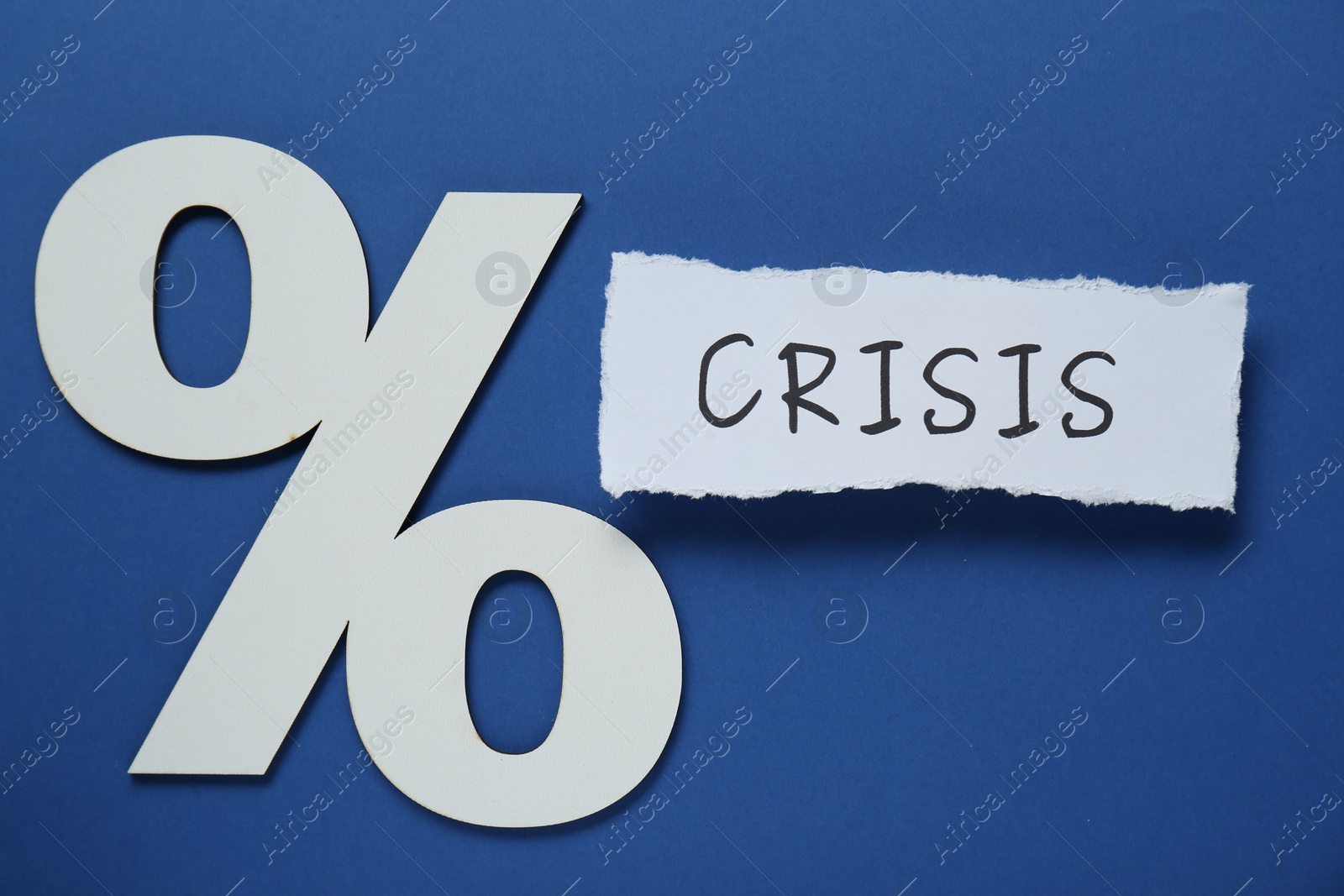 Photo of Paper piece with word Crisis and percent sign on blue background, flat lay