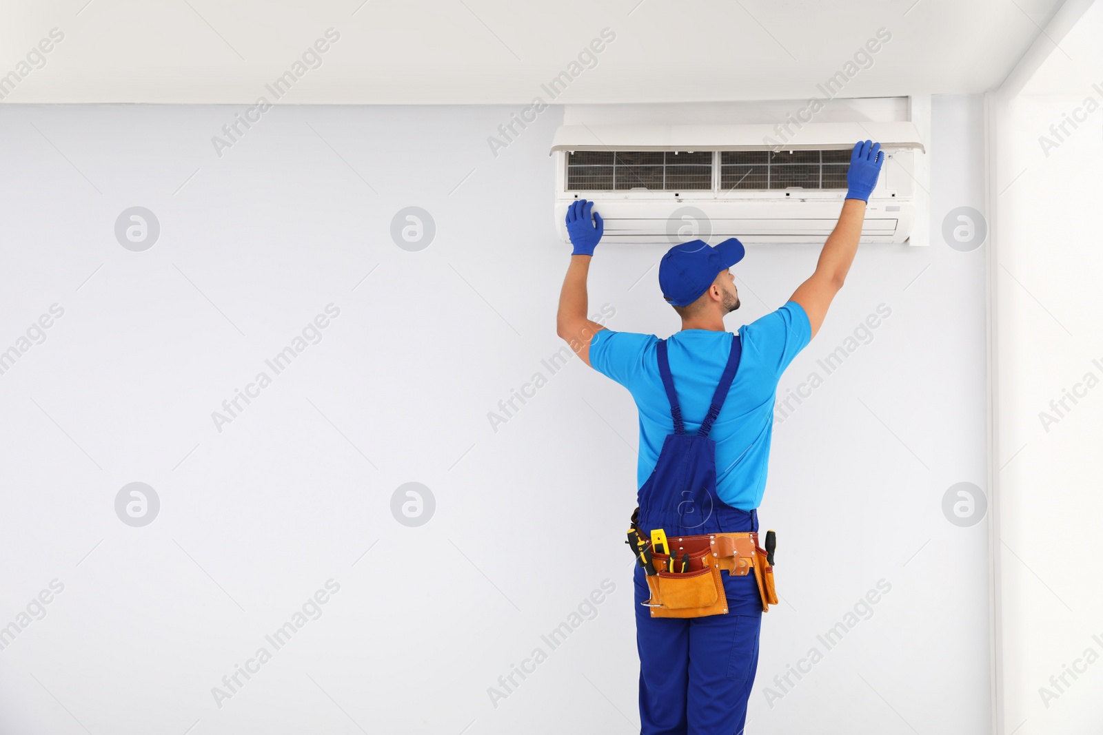 Photo of Professional technician maintaining modern air conditioner indoors. Space for text