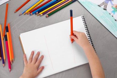 Little boy drawing with pencil at grey textured table, top view. Child`s art