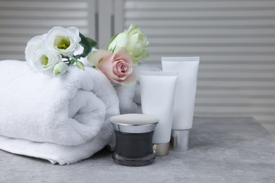 Photo of Towels, cosmetic products and flowers on grey table indoors