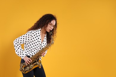 Beautiful African American woman playing saxophone on yellow background. Space for text