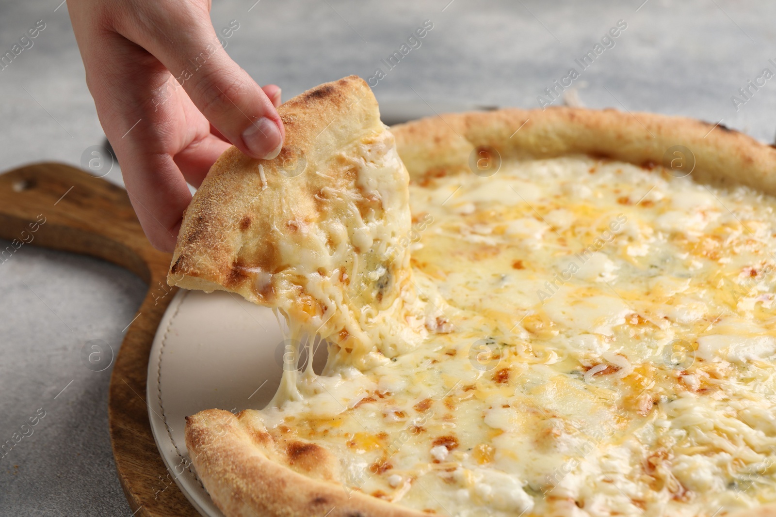 Photo of Woman taking piece of delicious cheese pizza at light grey table, closeup