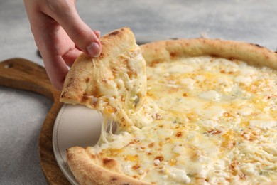 Woman taking piece of delicious cheese pizza at light grey table, closeup