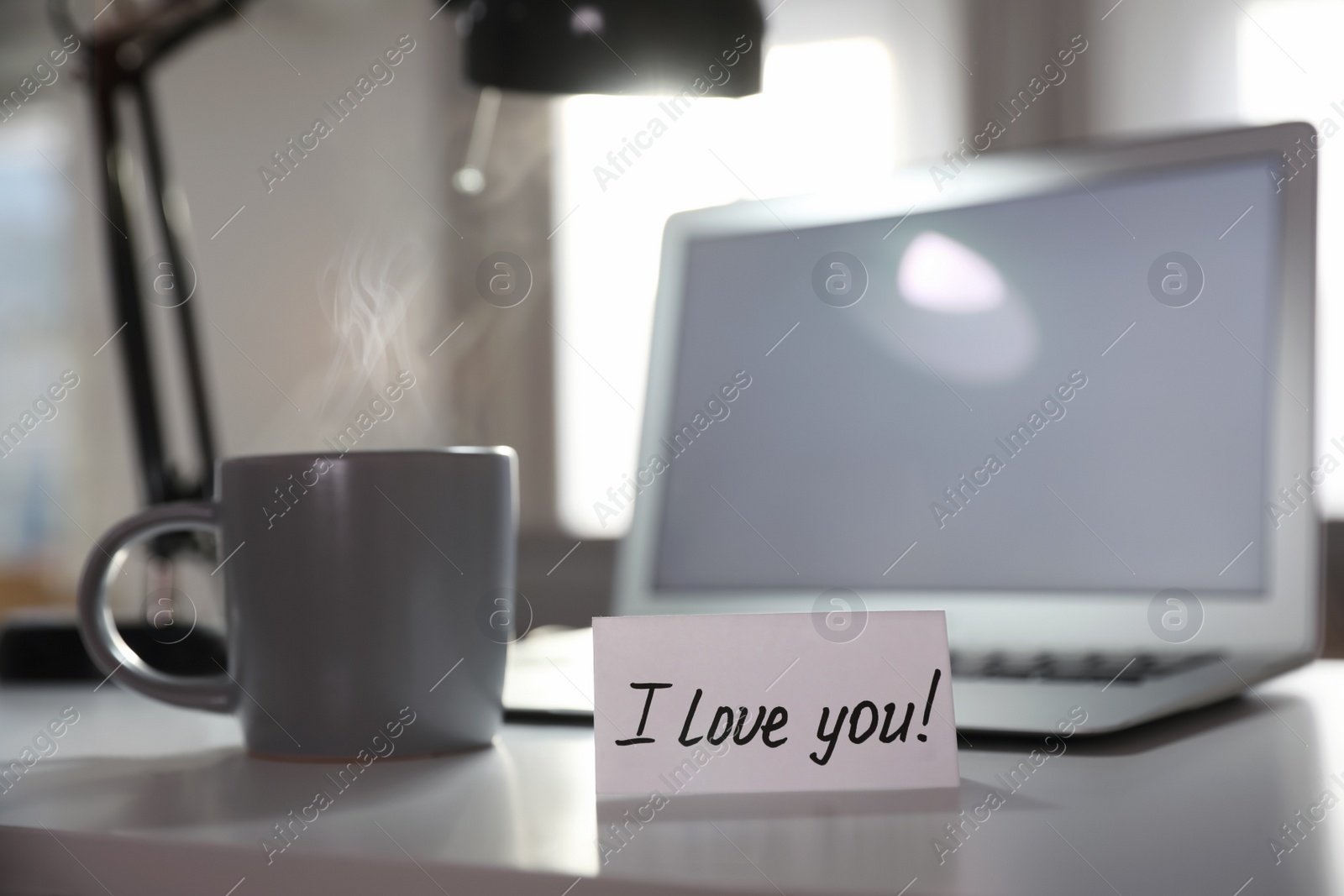Photo of Note with handwritten text I Love You on workplace indoors. Romantic message