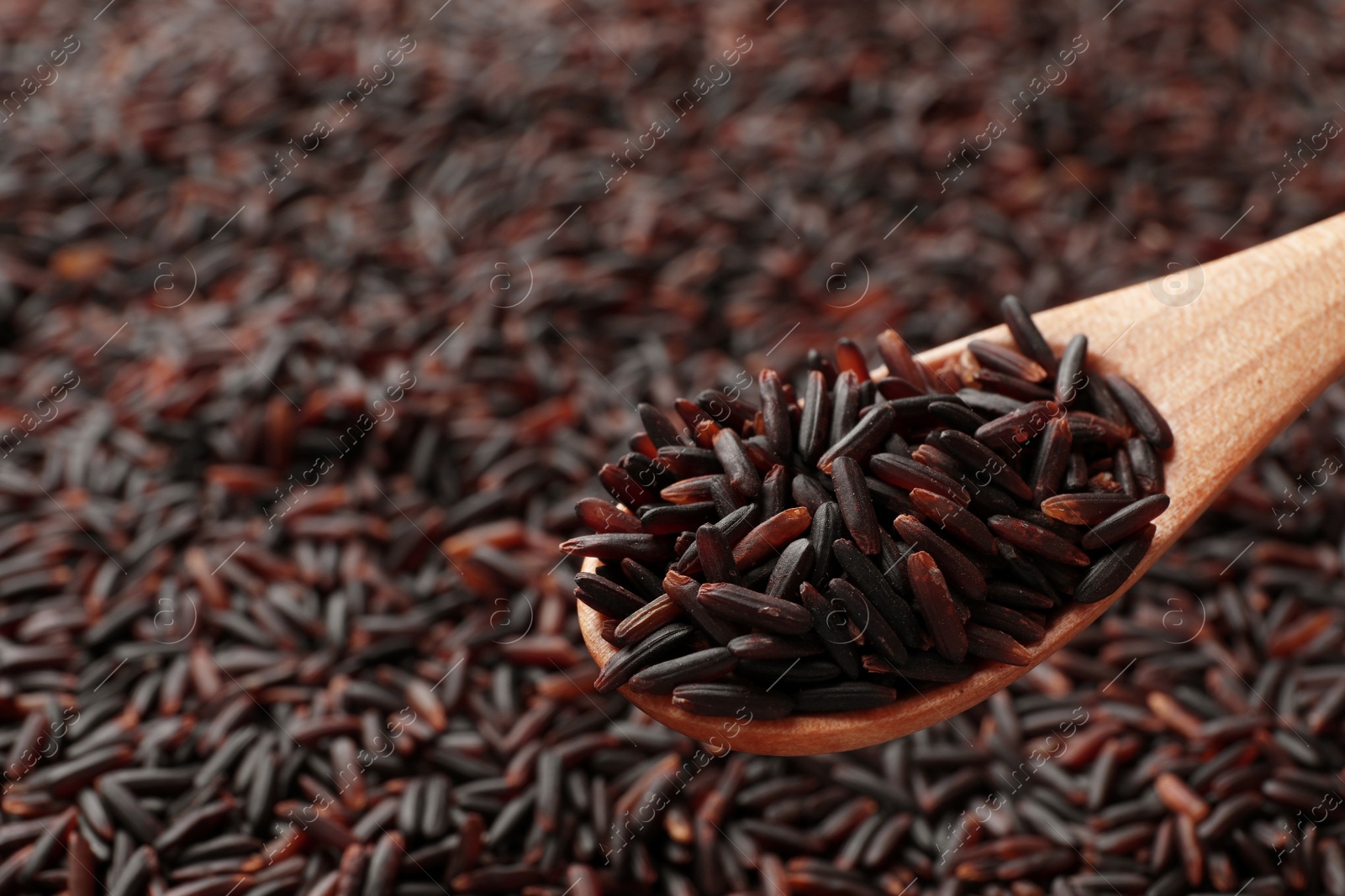 Photo of Wooden spoon with raw brown rice over cereal, closeup